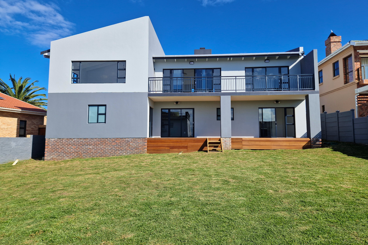 Modern two-story rear facade featuring a spacious lawn, timber decking, and a large balcony with sliding glass doors.
