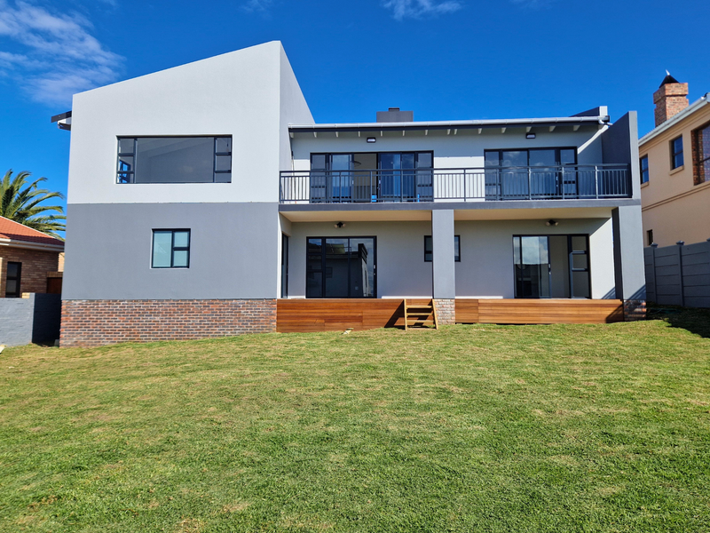 Modern two-story rear facade featuring a spacious lawn, timber decking, and a large balcony with sliding glass doors.