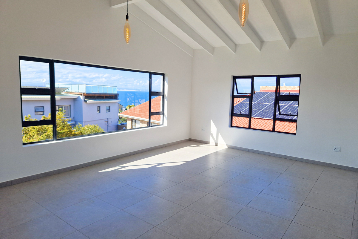 Bright and spacious living area featuring tiled floors, exposed beam ceilings, and large windows offering natural light and neighborhood views.