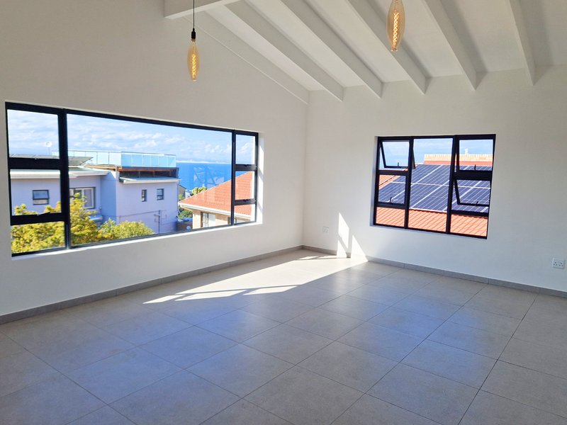 Bright and spacious living area featuring tiled floors, exposed beam ceilings, and large windows offering natural light and neighborhood views.