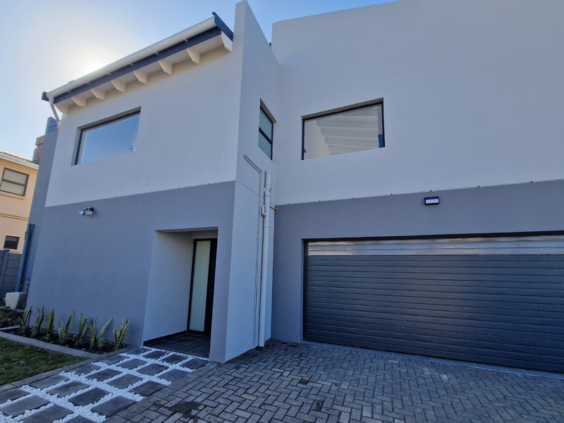 Modern double-story residential facade featuring a sleek grey and white exterior, integrated garage, and paved driveway with a landscaped entrance path.