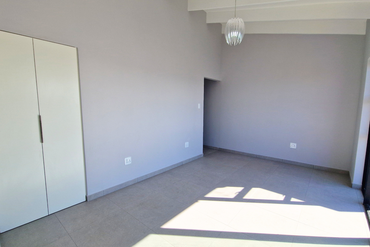 A bright, empty bedroom featuring neutral tiled flooring, built-in wardrobes, and exposed ceiling beams, offering a clean and versatile living space.
