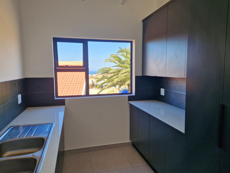 A modern, well-maintained scullery featuring dark cabinetry, quartz countertops, a double bowl sink, and a window with a pleasant exterior view.