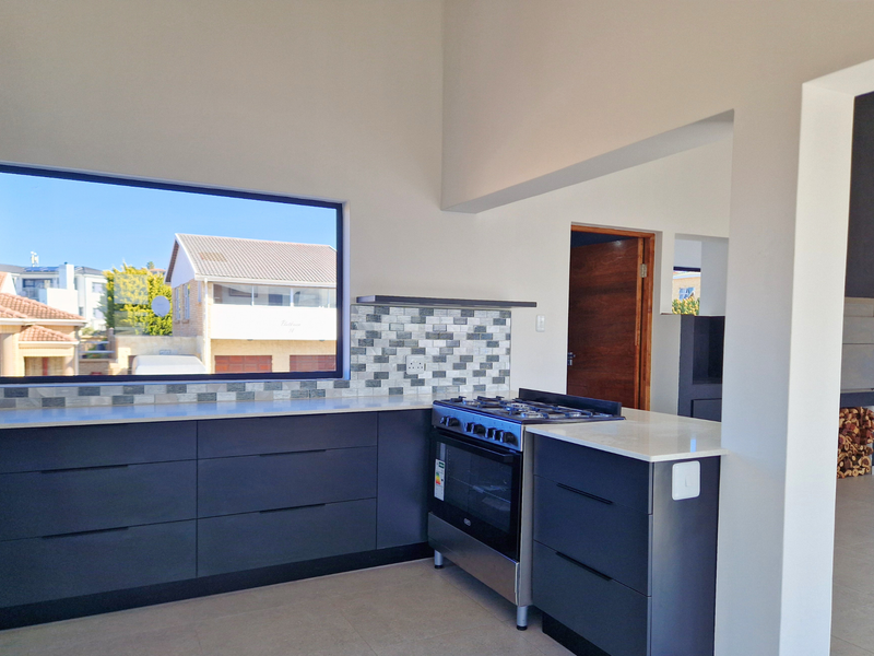 Modern kitchen featuring dark cabinetry, stone countertops, a gas stove, and a large window providing natural light and views.