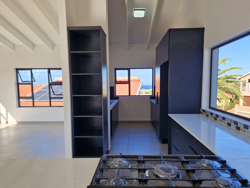 Modern kitchen featuring dark cabinetry, stone countertops, a gas hob, and a vaulted ceiling with views of the surrounding neighbourhood.