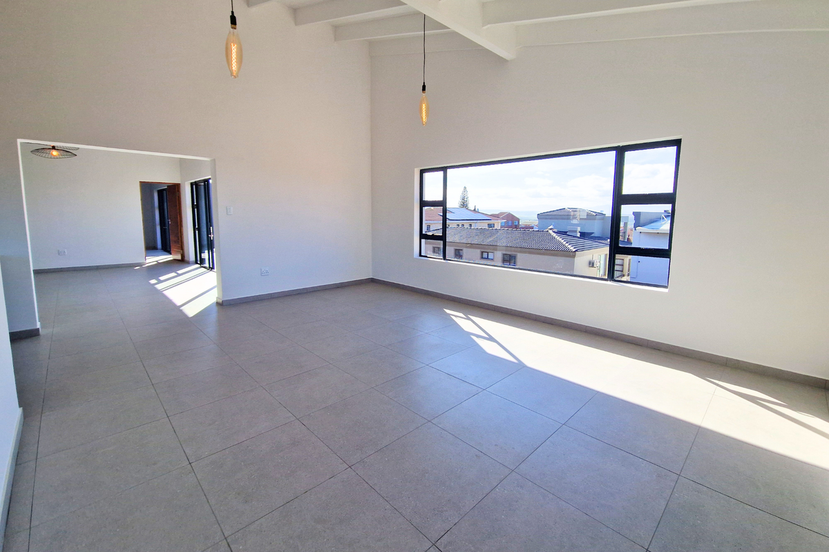 Spacious, light-filled living area featuring high exposed beam ceilings, modern tiled flooring, and a large window offering neighborhood views.