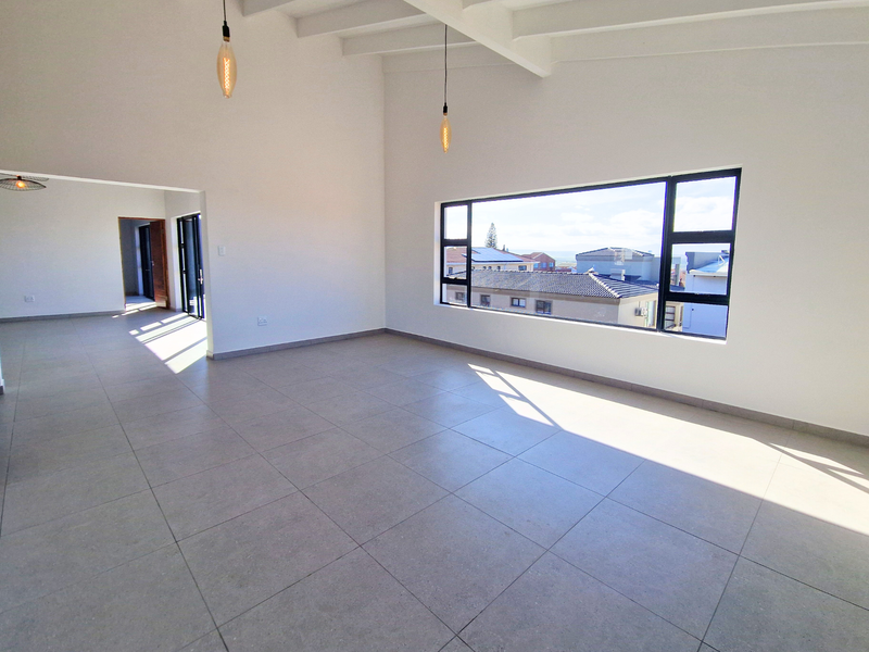 Spacious, light-filled living area featuring high exposed beam ceilings, modern tiled flooring, and a large window offering neighborhood views.
