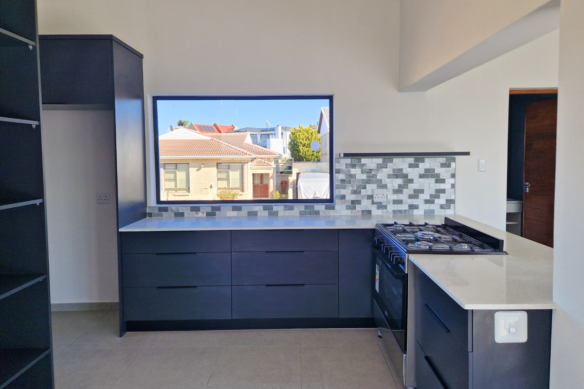Modern kitchen featuring dark cabinetry, stone countertops, a gas hob, and a tiled backsplash with a large window overlooking the neighborhood.