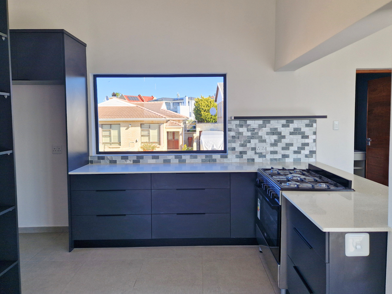 Modern kitchen featuring dark cabinetry, stone countertops, a gas hob, and a tiled backsplash with a large window overlooking the neighborhood.