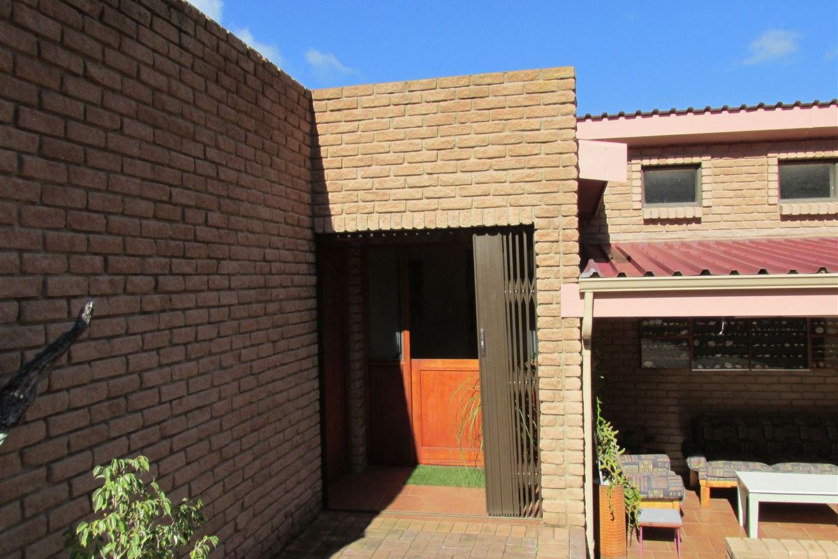 Rear exterior view featuring a face brick facade, tiled patio area, and a secure entrance with a metal security gate.