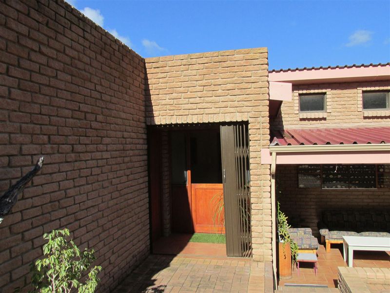 Rear exterior view featuring a face brick facade, tiled patio area, and a secure entrance with a metal security gate.