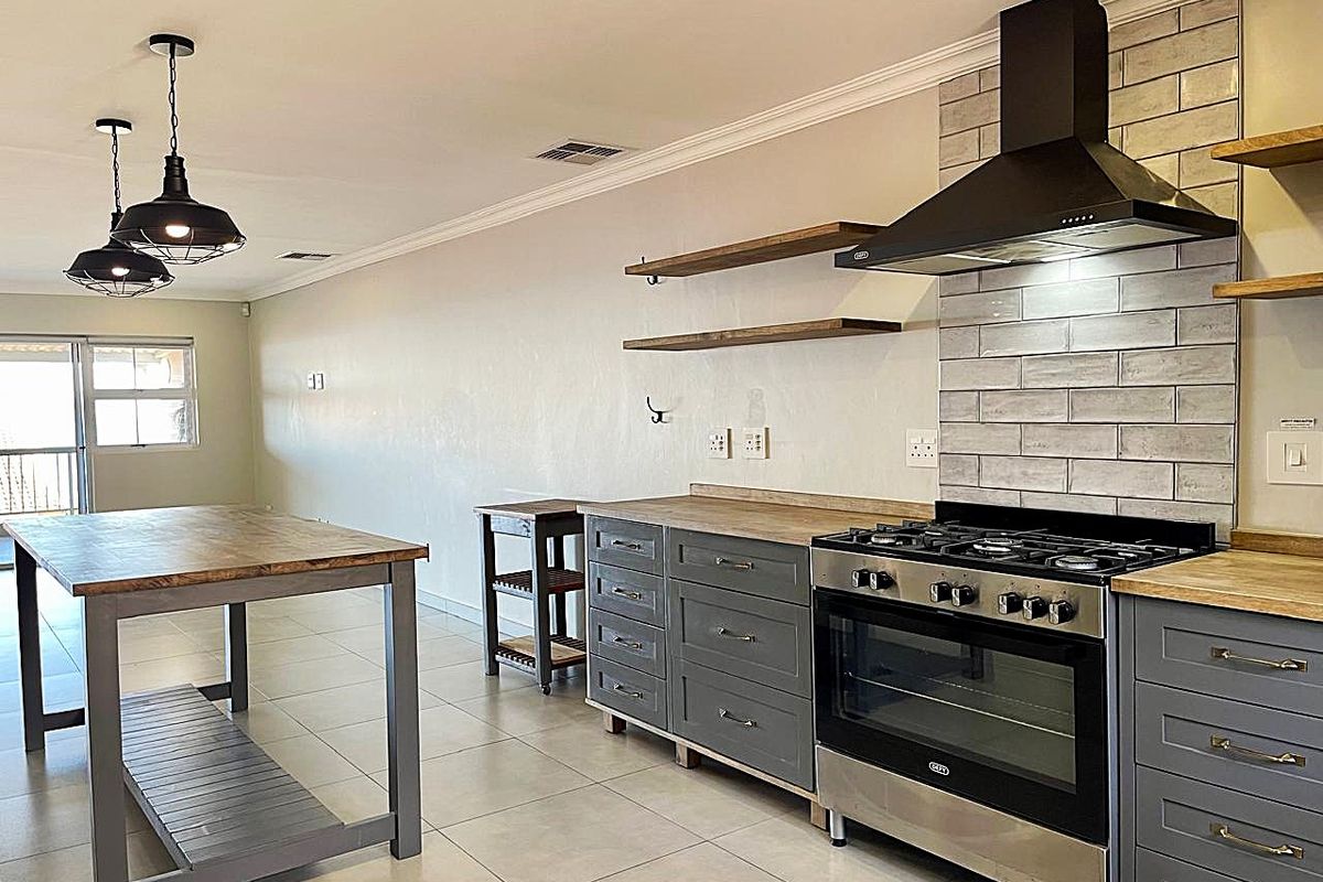 Modern kitchen featuring grey cabinetry, wooden countertops, tiled backsplash, gas stove with extractor fan, and stylish pendant lighting in an open-plan layout.