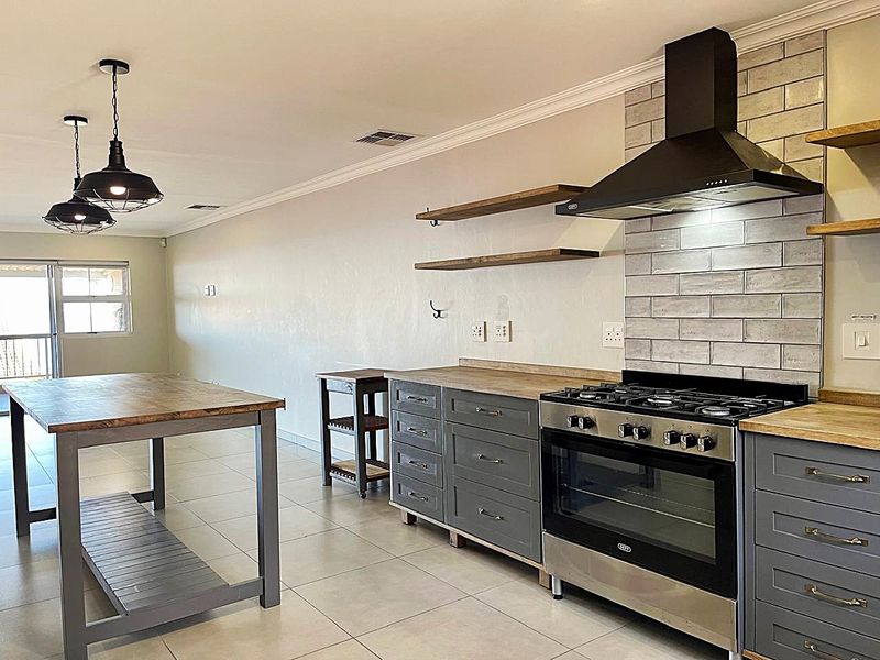 Modern kitchen featuring grey cabinetry, wooden countertops, tiled backsplash, gas stove with extractor fan, and stylish pendant lighting in an open-plan layout.