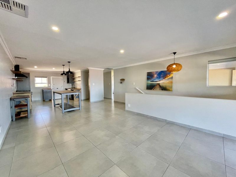 Spacious open-plan living and kitchen area featuring neutral tiled flooring, modern recessed lighting, and a functional kitchen layout with built-in cabinetry.