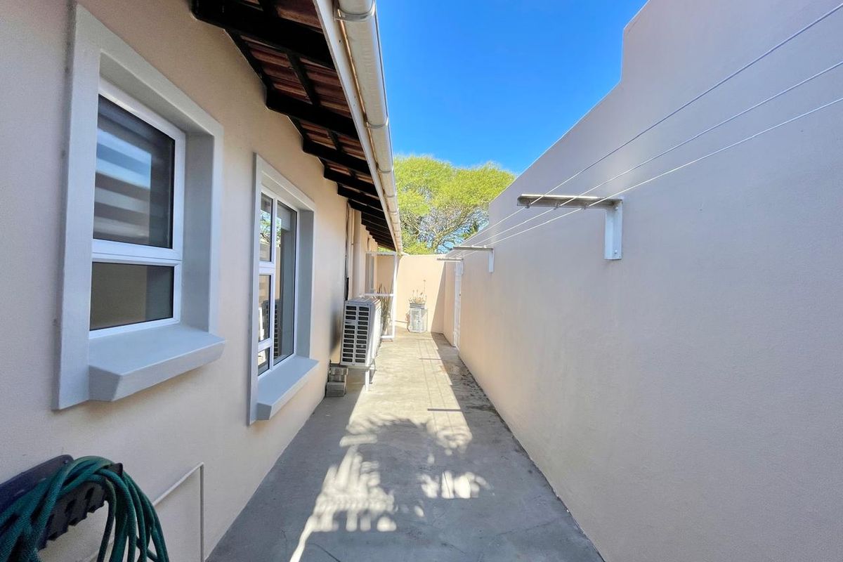 A narrow rear exterior walkway featuring concrete paving, a wall-mounted clothesline, and an external air conditioning unit.