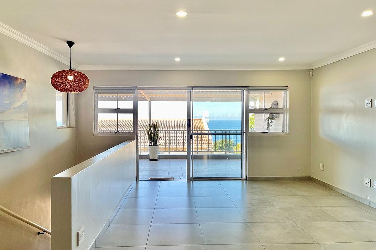 Bright and spacious living area featuring neutral tiled flooring, recessed lighting, and large sliding doors opening onto a balcony with ocean views.