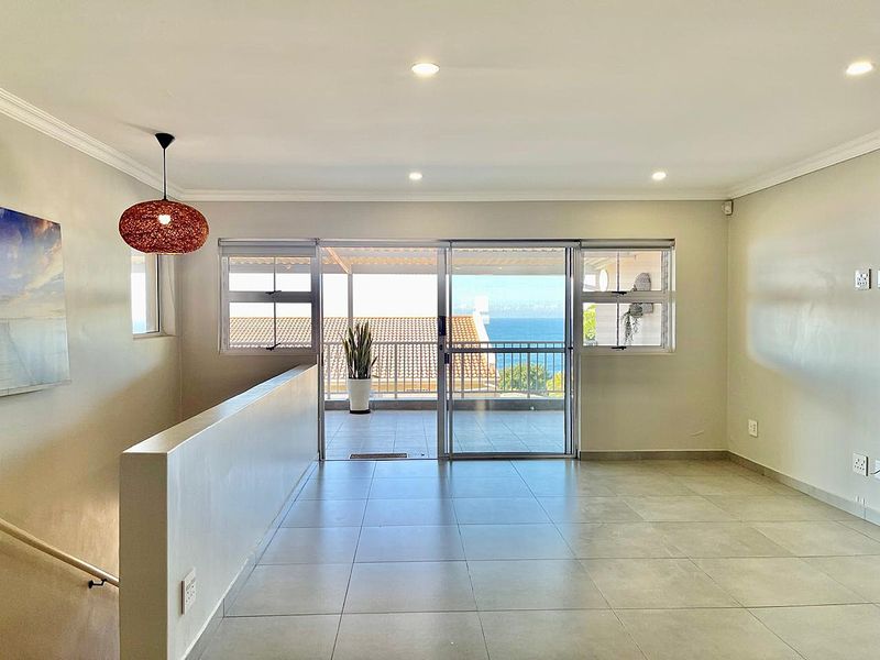 Bright and spacious living area featuring neutral tiled flooring, recessed lighting, and large sliding doors opening onto a balcony with ocean views.