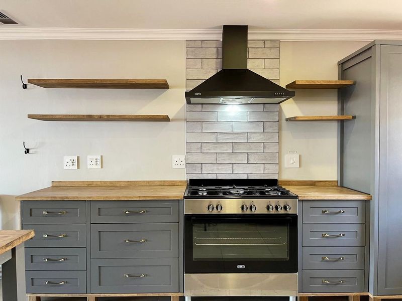 Modern kitchen featuring grey cabinetry, wooden countertops, a gas stove with extractor fan, and stylish subway tile backsplash with floating shelves.