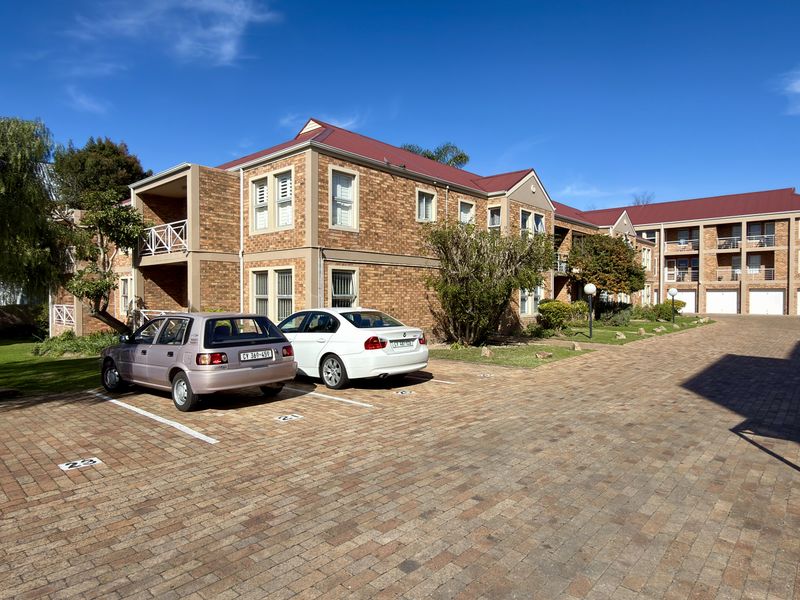 Exterior view of a multi-story brick apartment complex featuring a paved parking area, metal roofing, and private balconies.