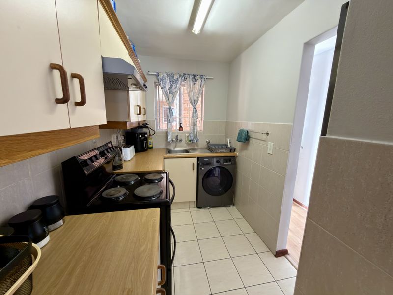 A functional kitchen featuring built-in cabinetry, an electric stove with extractor fan, double sink, and tiled finishes throughout.