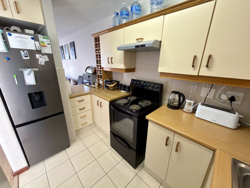 A functional kitchen featuring laminate countertops, built-in cabinetry, an electric stove with extractor fan, and tiled flooring.