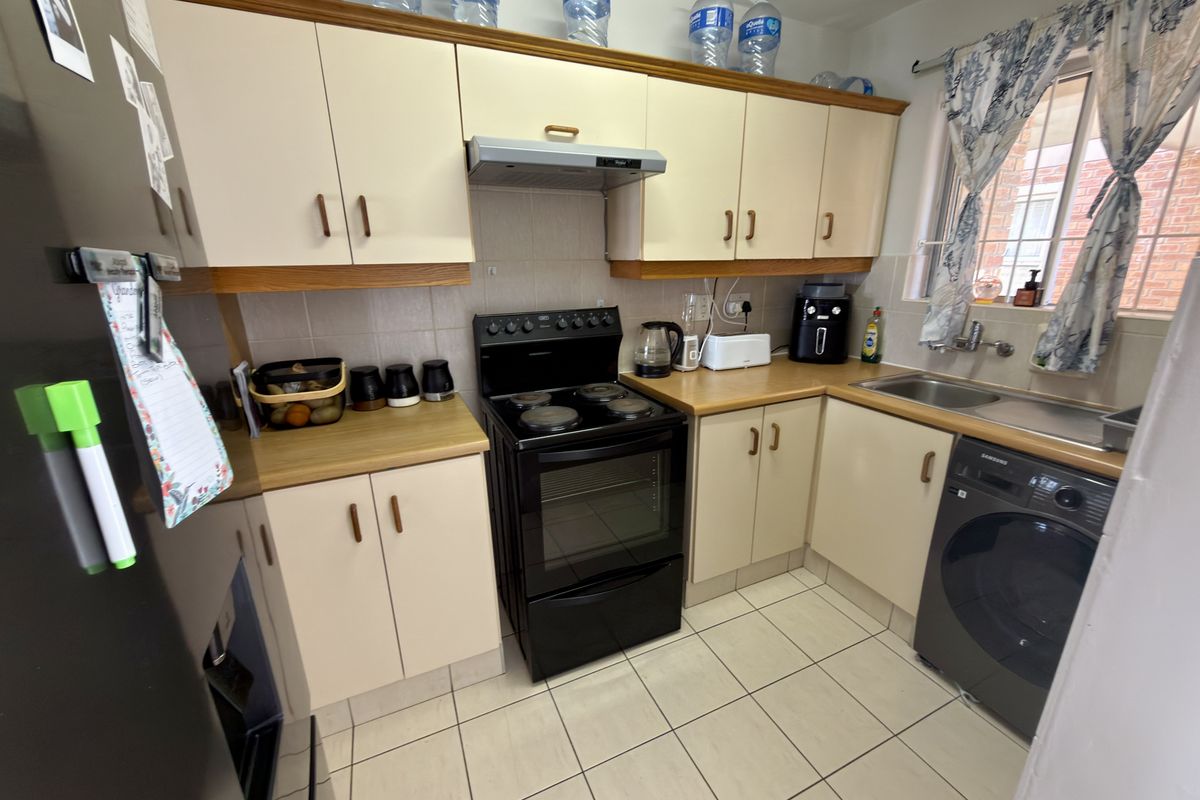 A functional kitchen featuring laminate cabinetry, a built-in electric stove with extractor fan, tiled flooring, and a stainless steel sink.