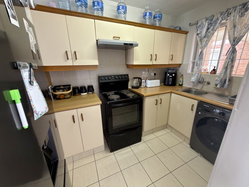A functional kitchen featuring laminate cabinetry, a built-in electric stove with extractor fan, tiled flooring, and a stainless steel sink.