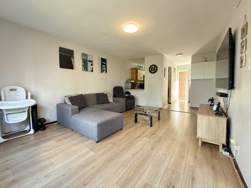 Open-plan living area featuring light-toned laminate flooring and a pass-through window connecting to the kitchen space.