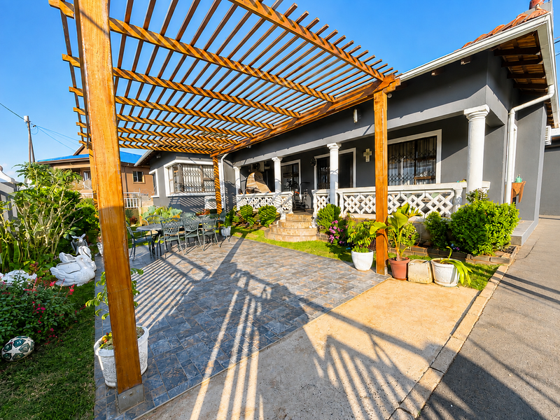 A well-maintained outdoor patio featuring a large wooden pergola, decorative balustrades, and tiled flooring, providing a comfortable space for outdoor relaxation.