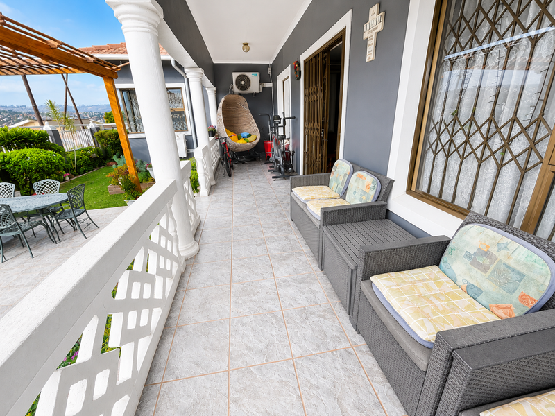 A spacious covered patio featuring tiled flooring, decorative columns, and a wooden pergola, overlooking a landscaped garden area.
