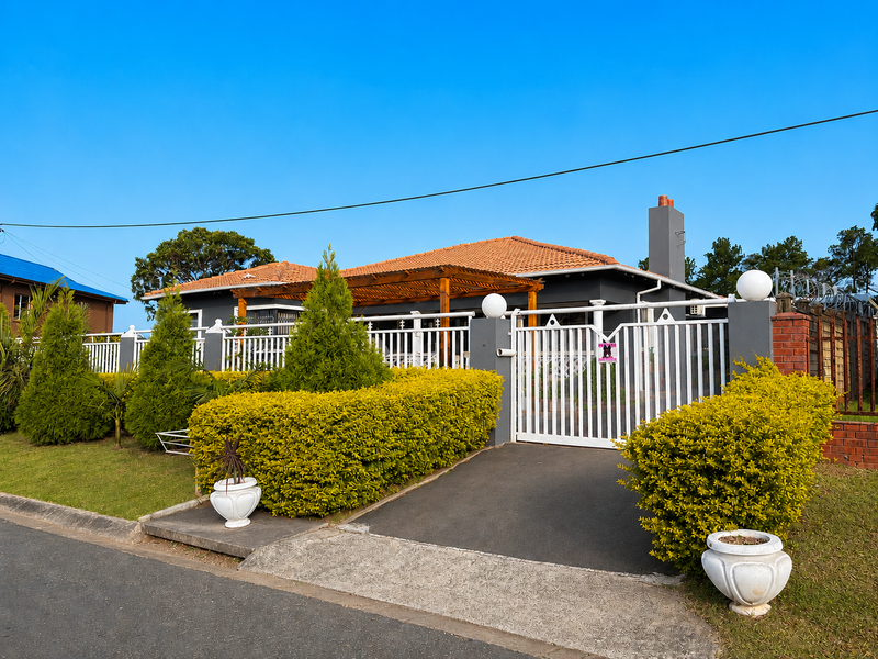 Front view of a well-maintained house featuring a tiled roof, timber pergola, and secure metal gate with a paved driveway.