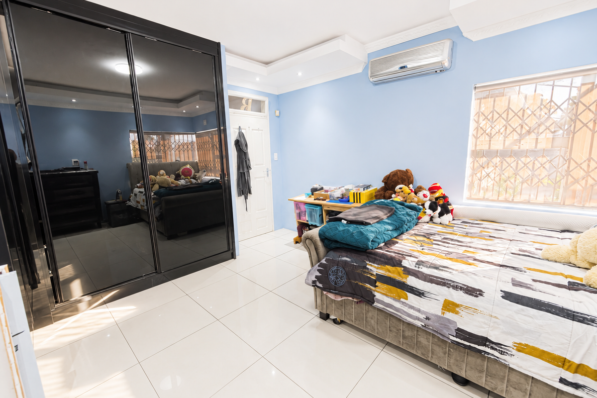 A well-maintained bedroom featuring large mirrored built-in wardrobes, tiled flooring, a split-system air conditioner, and decorative ceiling bulkheads.