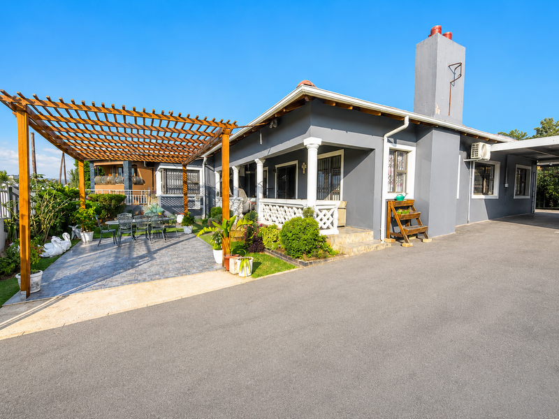 Rear exterior view featuring a paved patio area with a wooden pergola, chimney stack, and asphalt driveway access.