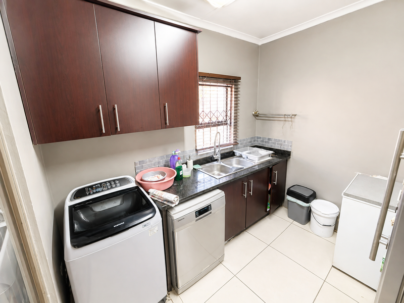 A functional laundry room featuring dark wood cabinetry, a double basin sink, tiled backsplash, and tiled flooring with space for appliances.