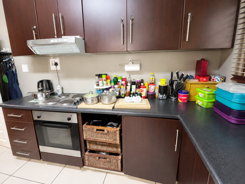 A functional kitchen featuring dark wood cabinetry, a built-in oven with electric hob, extractor fan, and practical pull-out storage baskets.