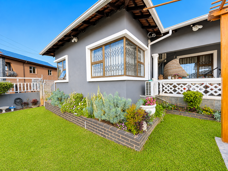 A well-maintained rear exterior view featuring a landscaped brick planter box, a covered patio area with a timber pergola, and secure window fittings.