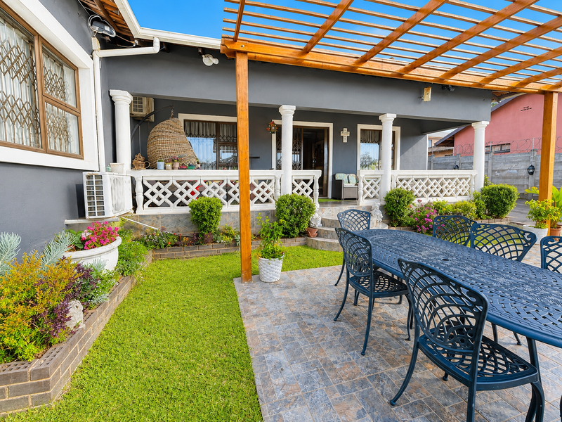A well-maintained covered patio area featuring a wooden pergola, decorative balustrades, and tiled flooring, overlooking a neat garden space.