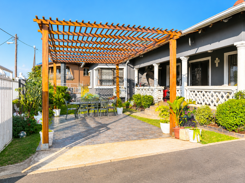 A well-maintained outdoor patio area featuring a large wooden pergola, tiled flooring, and decorative balustrades, providing a pleasant space for outdoor relaxation.