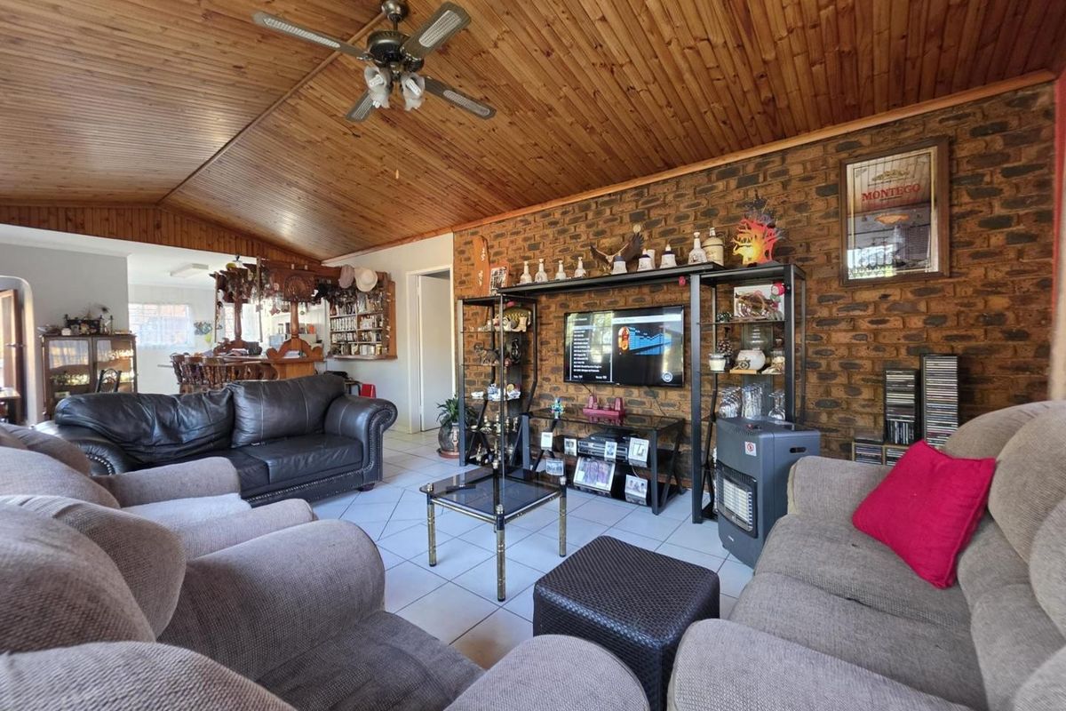 Spacious living room featuring a rustic exposed brick wall, timber-clad vaulted ceiling with a fan, and neutral tiled flooring.