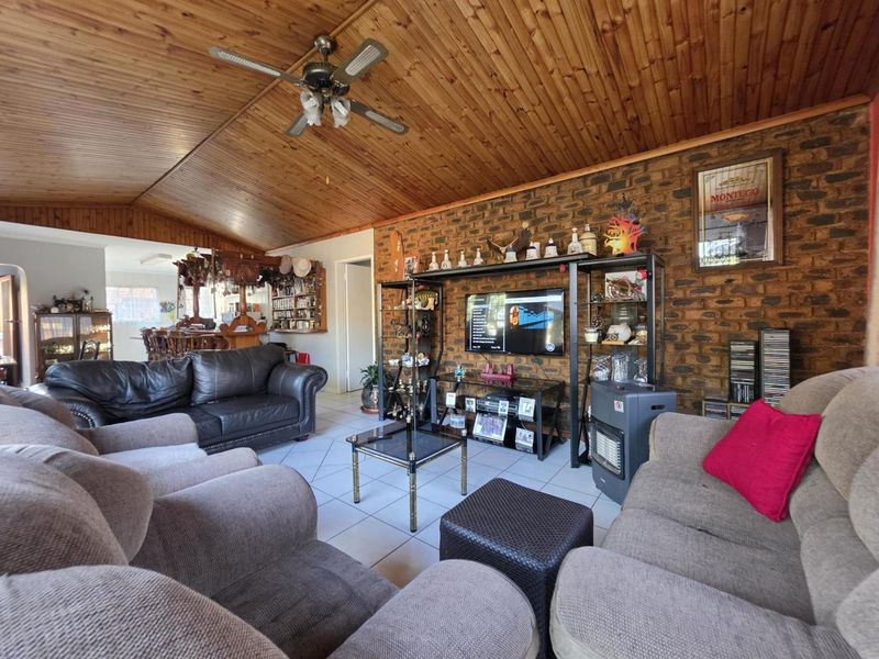 Spacious living room featuring a rustic exposed brick wall, timber-clad vaulted ceiling with a fan, and neutral tiled flooring.