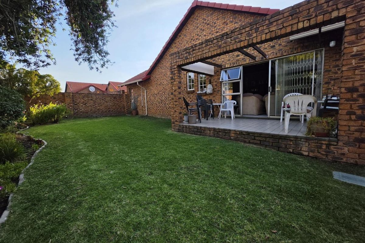 A rear view of the townhouse featuring a covered brick patio, sliding glass doors, and a private garden with a brick boundary wall.