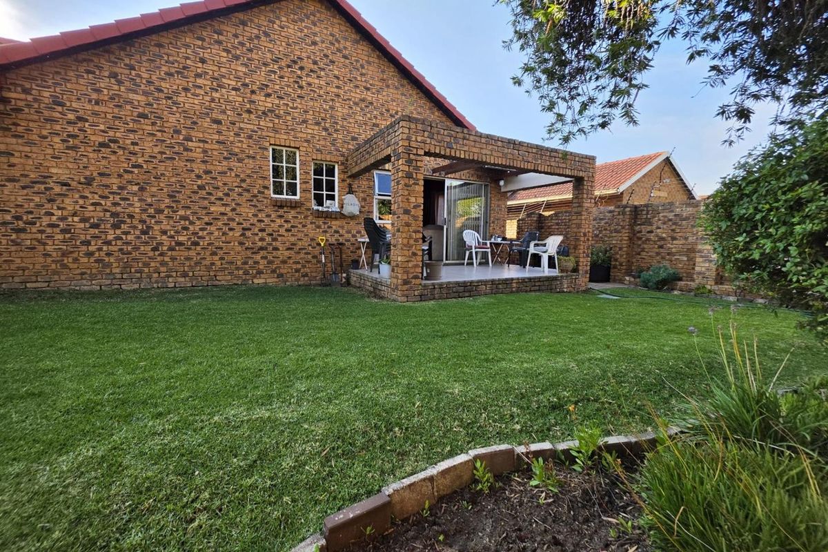 Rear view of the townhouse featuring a face-brick facade, a covered patio area, and a well-maintained private garden with a brick boundary wall.