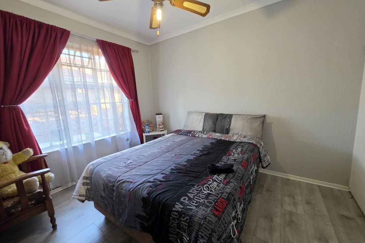 A functional bedroom featuring laminate flooring, a ceiling fan, and large windows with security bars, providing a comfortable and well-lit living space.