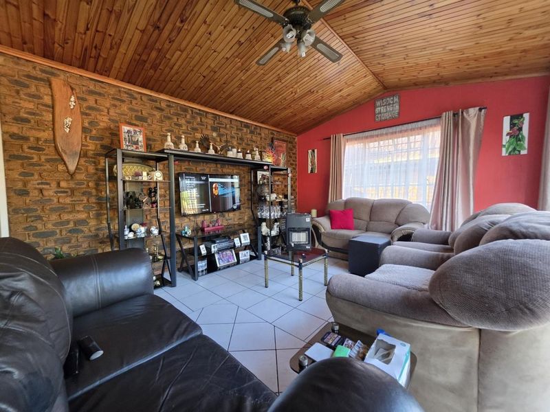 A living room featuring an exposed brick feature wall, a vaulted timber ceiling with a fan, and tiled flooring.