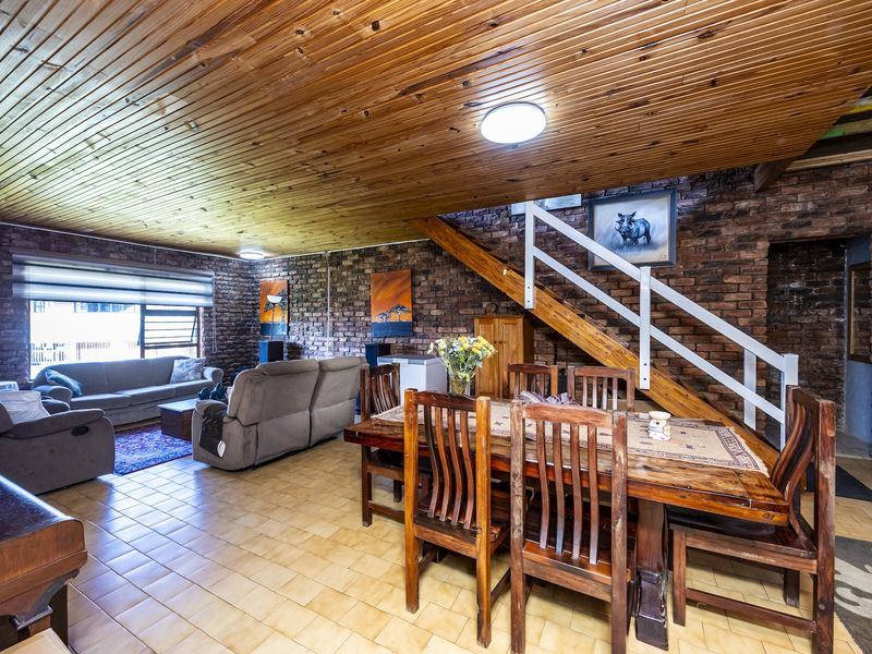 Spacious open-plan living and dining area featuring rustic exposed brick walls, a timber-clad ceiling, and a central staircase.