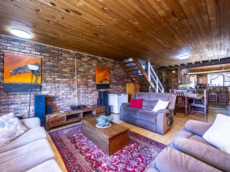 Spacious open-plan living and dining area featuring exposed brick walls, a timber-clad ceiling, and a staircase leading to the upper level.