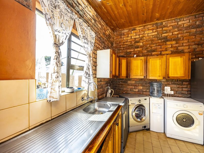 Functional laundry area featuring exposed brick walls, timber ceiling, stainless steel sink, and wooden cabinetry with tiled splashback.