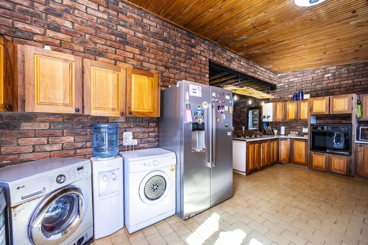 Spacious kitchen featuring exposed brick walls, timber ceiling, and extensive wooden cabinetry with integrated oven and hob.