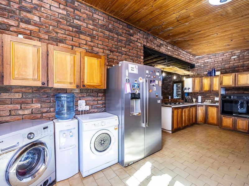 Spacious kitchen featuring exposed brick walls, timber ceiling, and extensive wooden cabinetry with integrated oven and hob.