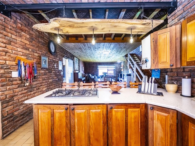 Open-plan kitchen featuring exposed brick walls, timber cabinetry, stone countertops, and a gas hob, overlooking the living area with an industrial aesthetic.